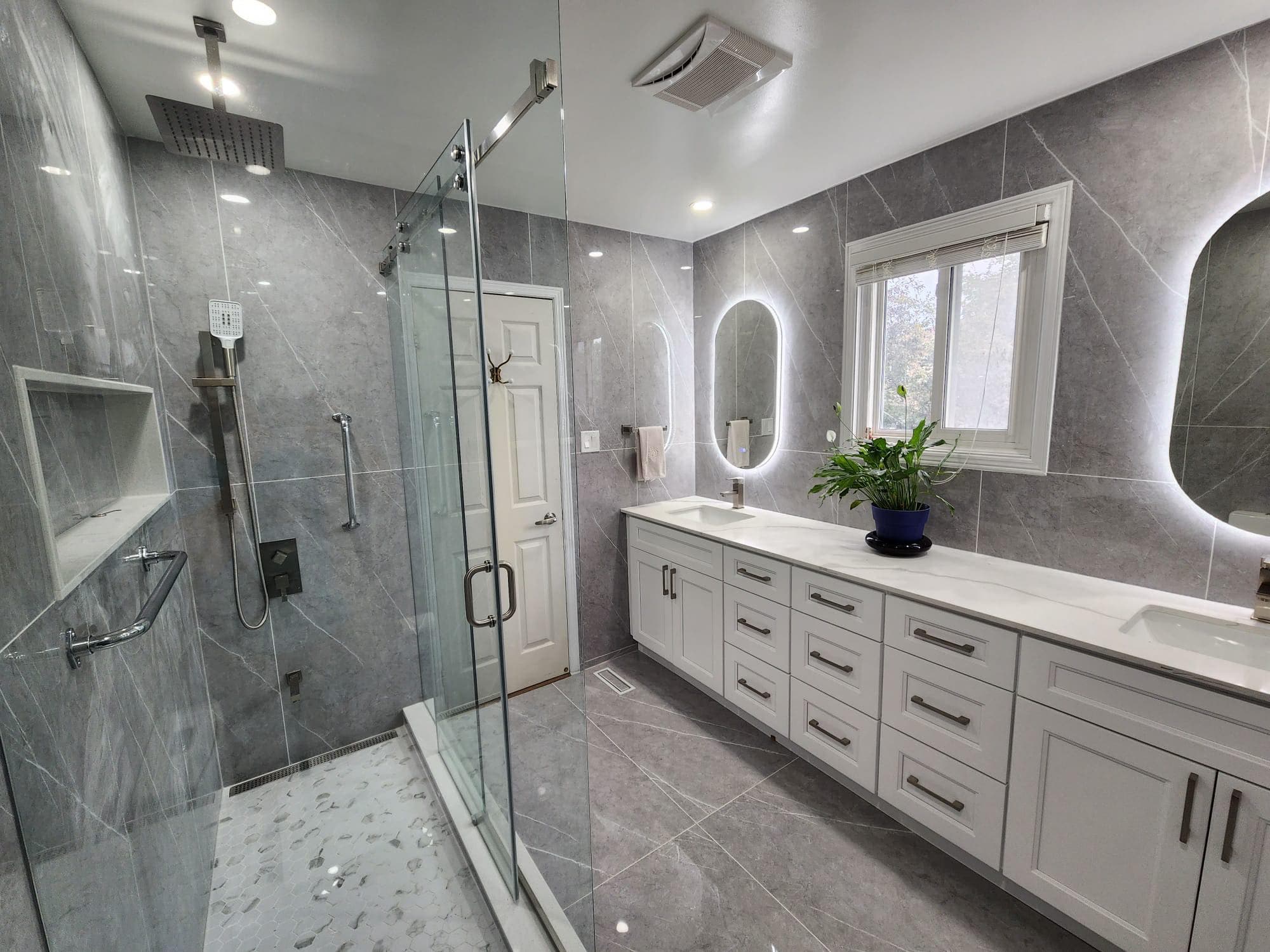 Modern bathroom with gray marble tiles, glass-enclosed shower, and white double vanity with backlit mirrors.
