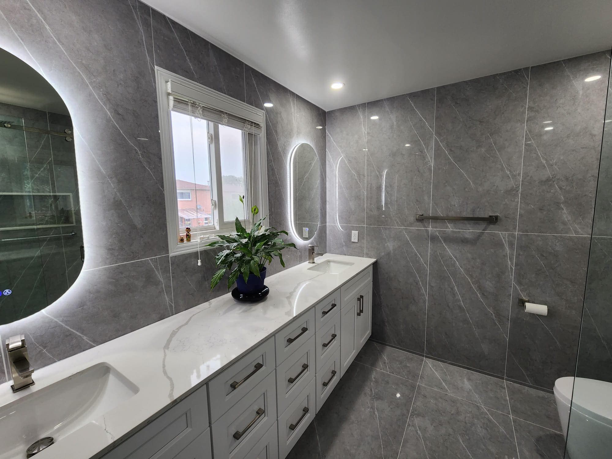 Modern grey marble bathroom with a white double vanity and two backlit oval mirrors.