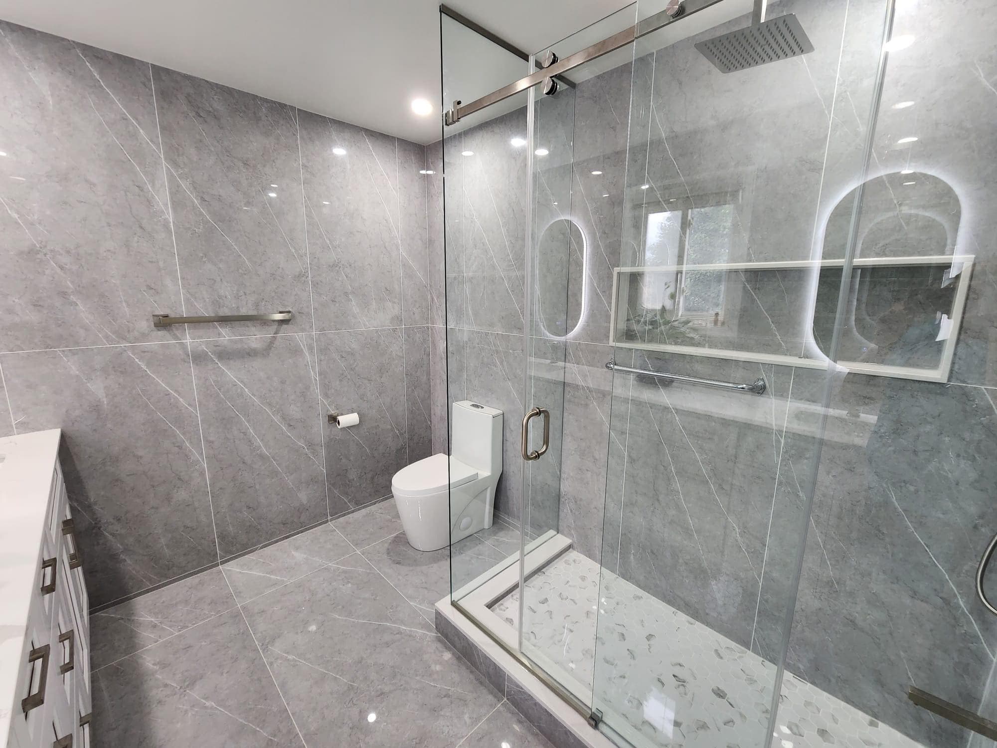 Modern grey marble bathroom featuring a glass walk-in shower, pebble floor, and white toilet.