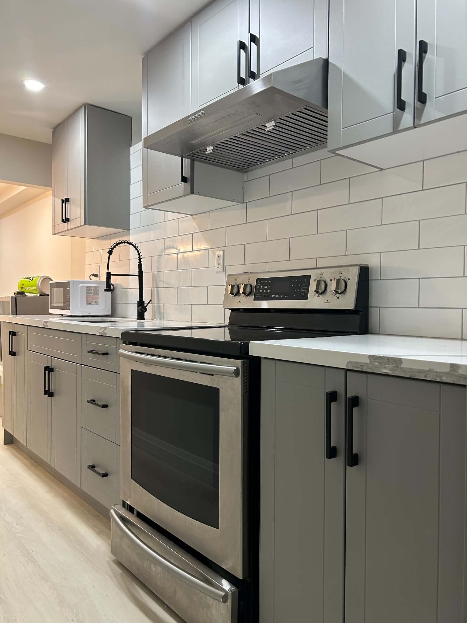 Grey kitchen cabinets, white subway tile backsplash, and stainless steel appliances with black hardware.