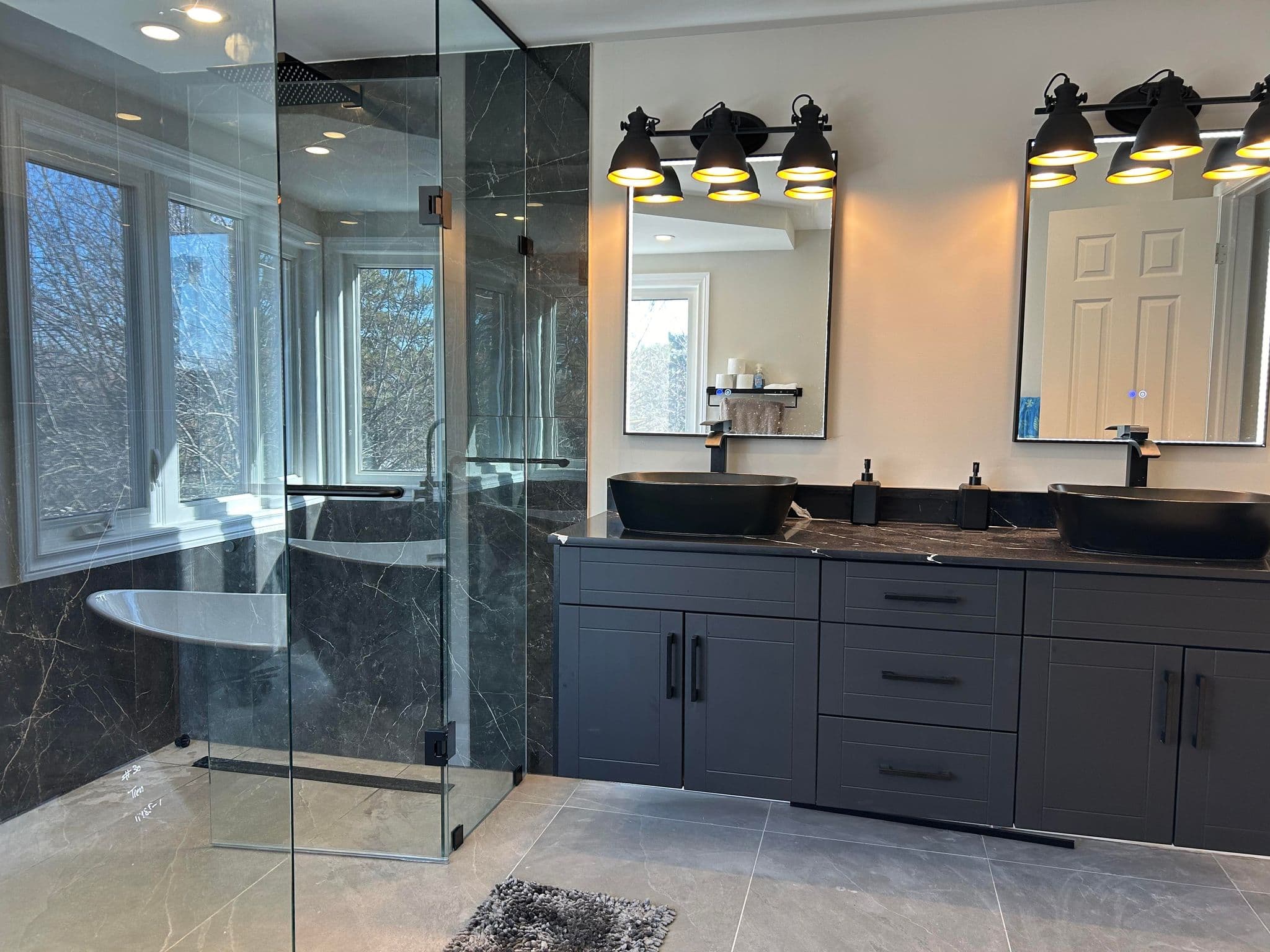 Modern bathroom with dark grey double vanity, black vessel sinks, and a large glass shower.