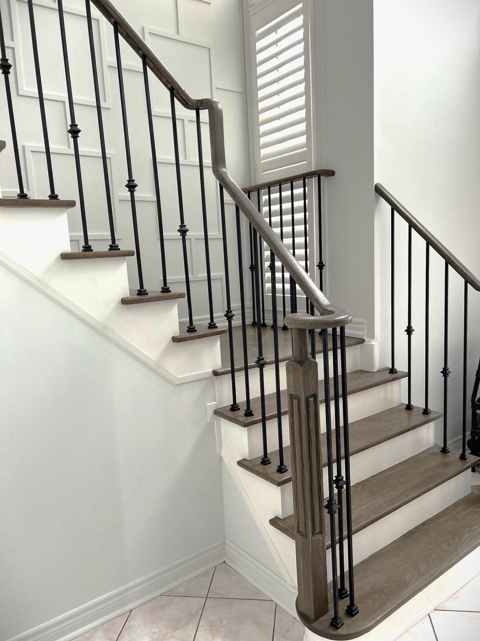 Modern staircase with dark wood treads, white risers, black metal balusters, and curved handrail.